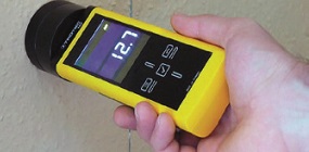 A microwave moisture meter taking a reading from the wall