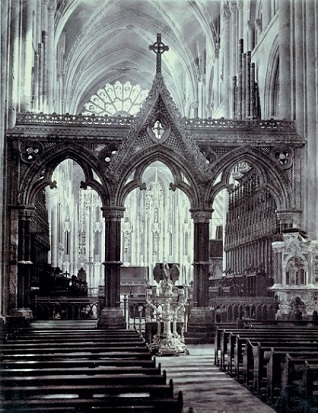 Historic b/w photo of cathedral interior with lectern in dominant central position lookig down aisle and with elaborate screen behind it