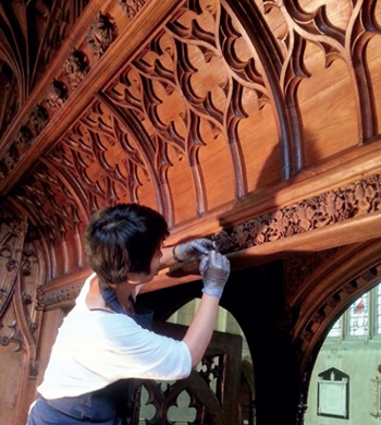 A conservator works on a richly carved historic timber screen