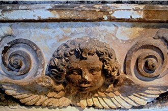 Pocked stone surface above carved head and wing motif