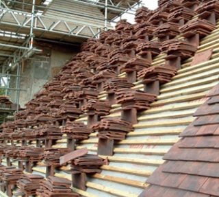Partially laid clay tile roof with unlaid tiles stacked at intervals