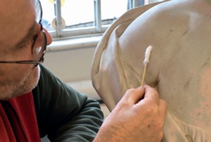 A conservator uses a cotton wool swab on the shoulder of a marble bust