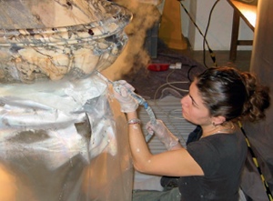 A conservator directs the nozzle of a portable steam cleaner close to the surface of a marble font