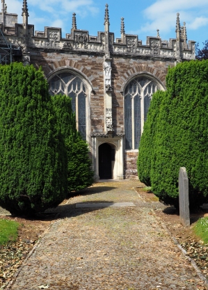A wide, tree-lined cobbled path leads through a churchyard to a porch