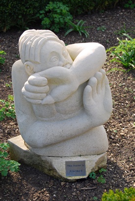 Sculpture of a stylised male figure in a defensive posture with one hand raised palm outwards and other arm covering lower face