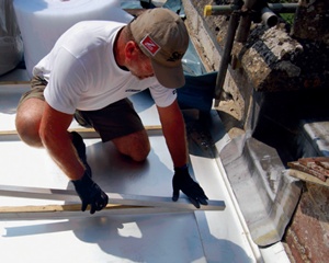 A roofer fits a new square stainless steel roofing 'roll' near a stone parapet