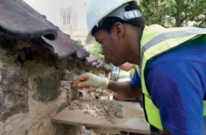 An apprentice applies a repair mortar to a masonry garden wall