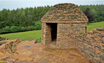 Circular stone shelter with corbelled roof and woodland in background