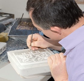 A craftsman hand carves patterns into a plaster mould with a pointed metal tool