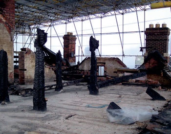Fire-damaged building beneath protective structure of scaffolding and waterproof sheeting