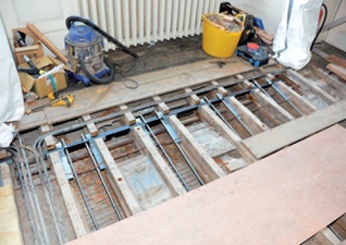 Lifted floorboards reveal threaded steel tensioning bars running parallel to the joists