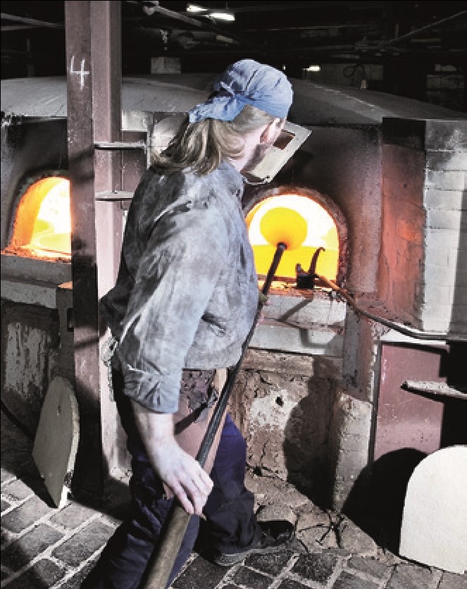 A glass-blower picking up the viscous glass mass onto the blowpipe and holding it in the furnace