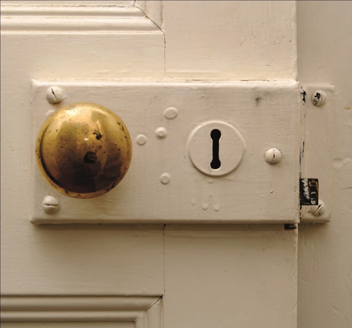 Close-up of a white historic door and its aging cold-coloured knob handle
