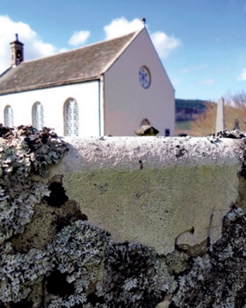 Close-up showing detail of lichen growth on headstone with church in the background