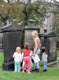 An adult and a group of children read the inscription on an old gravestone