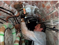 A member of the NT direct labour team seals pipework and cabling breaches in a brick-lined tunnel