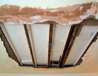 Large hole in plaster ceiling revealing laths and joists