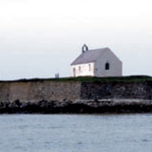 View of the limewashed church and the walled island from the shore