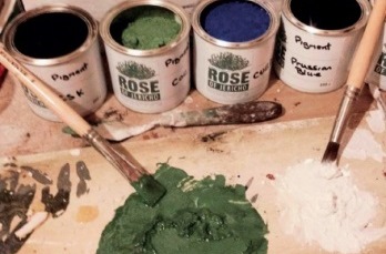 Open tins of dry pigment with brushes and mixed paint paste in foreground
