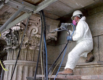 A conservator in protective clothing spray cleaning ornate column capital