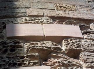 Stone repair: two replacement stones standing proud of adjacent eroded stones with faces in same plane as original wall face