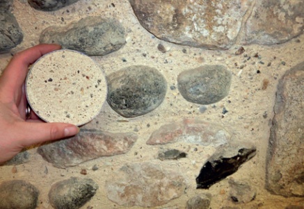 Close-up showing mortar biscuit being held up in front of rubble stone wall pointed with matching mortar