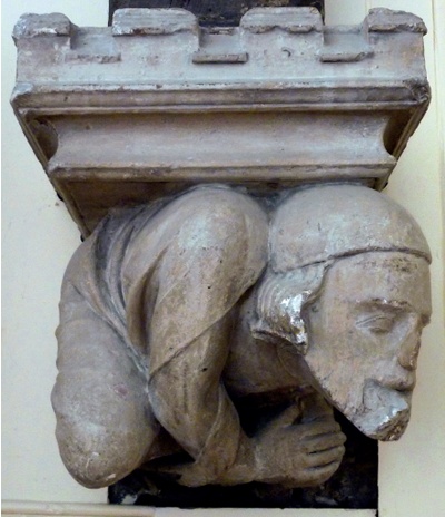 Atlas-style corbel comprised of a hunched figure bearing a castellated structure on his back