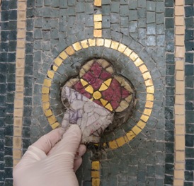 Adhesive fabric is peeled away from a small decorative element of the mosaic