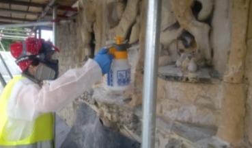 A conservator in protective clothing hand sprays the surface of the stone crest
