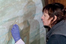 A conservator cleans an area of wall painting with a swab