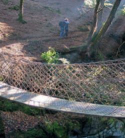 Restored chain bridge over the Ystwyth Gorge with walkers in woodland on the far side