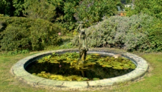 Circular, stone-edged pond with lily pads and statue at centre