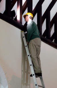 Man in a hard-hat inspecting church timberwork from the top of a ladder