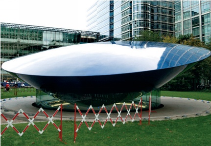 Very large, dish-shaped sculpture with modern office blocks behind