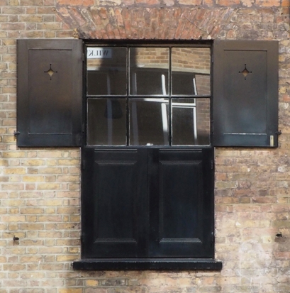 Sash window with split external shutters (top halves open to admit light, bottom closed for privacy/security)