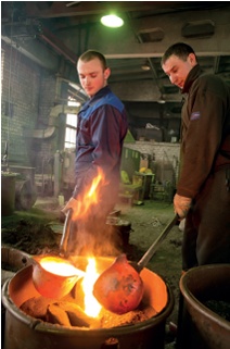 Foundry workers pour molten metal into a cast