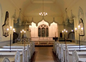 View of the church interior with its pale blue and white colour scheme, pendant ogee arches and blue and white pews with quatrefoils embellishing the pew ends