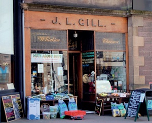 JL Gill shopfront with 'Whiskies' and 'Cheeses' painted in elaborate gold lettering on opaque and textured clerestorey glass