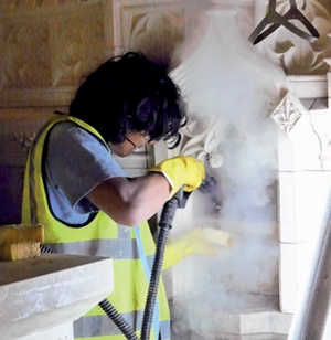 A conservator steam cleaning a carved stone niche