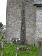 Stone cross in churchyard with church building behind it