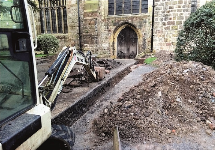 A mechanical digger creating a drainage trench in St Oswald's churchyard.