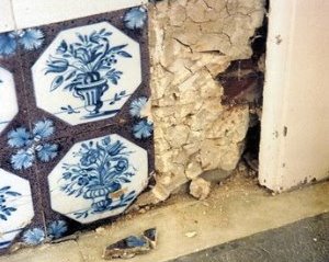 Small area of tile work with two tiles missing exposing badly cracked plaster backing